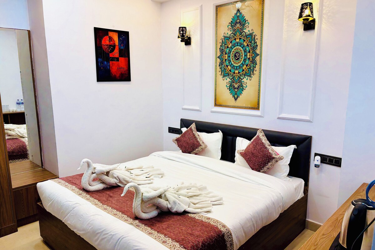 A neatly made bed with white linens and two swan-shaped towels, a large decorative wall piece, and a wall-mounted light fixture.