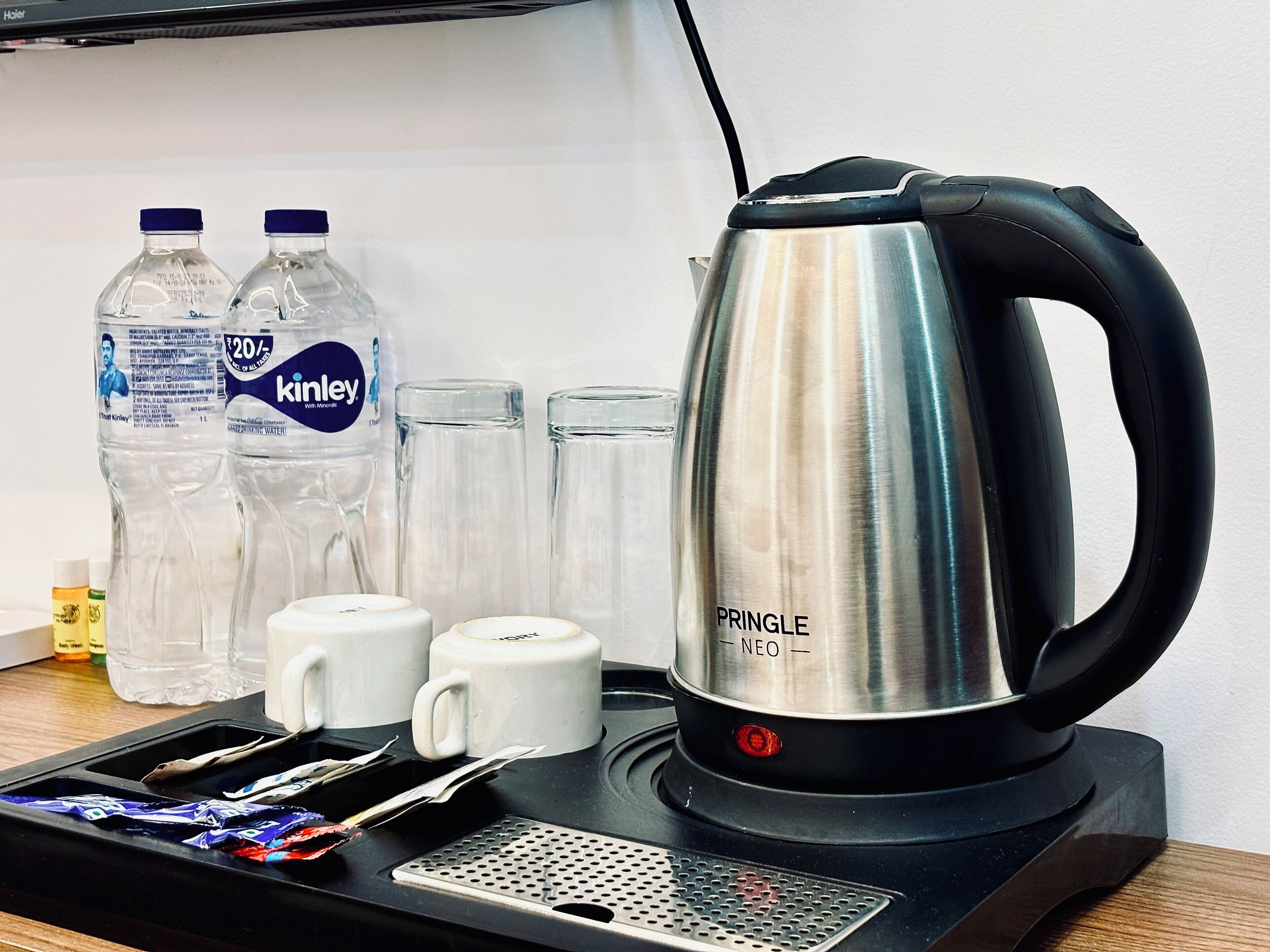 Eine Küchenzeile mit Wasserkocher, zwei Wasserflaschen, zwei Kaffeetassen und einer Ablage mit Portionspackungen.