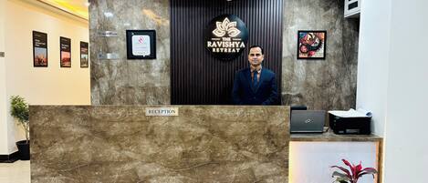 A reception desk with a marble top, a sign for "The Ravishya Retreat," and framed pictures on the wall.