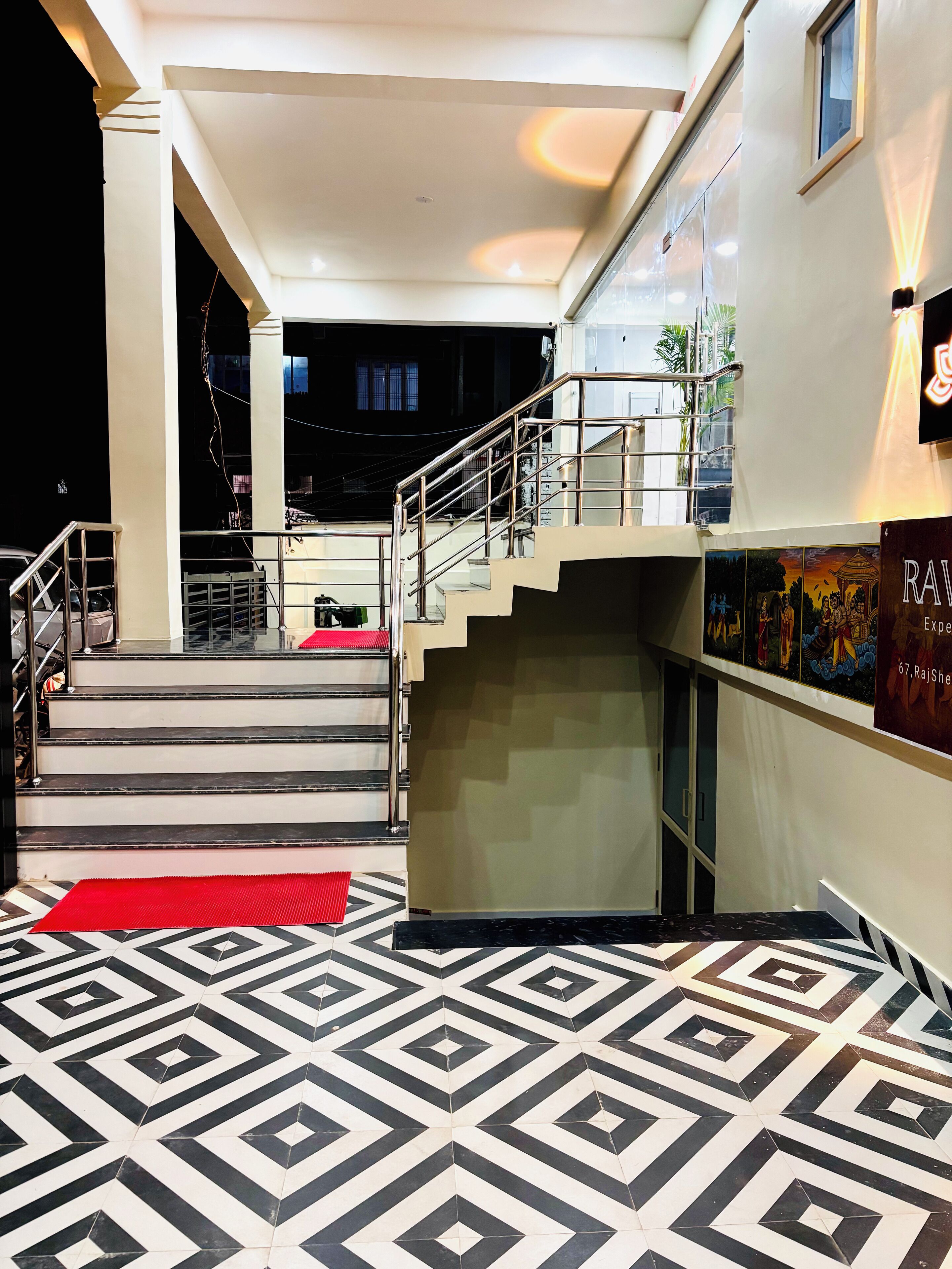 A hotel lobby with a geometric patterned floor, a staircase with metal railings, and a wall-mounted poster.