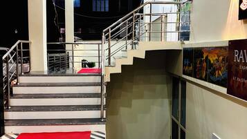 A hotel lobby with a geometric patterned floor, a staircase with metal railings, and a wall-mounted poster.