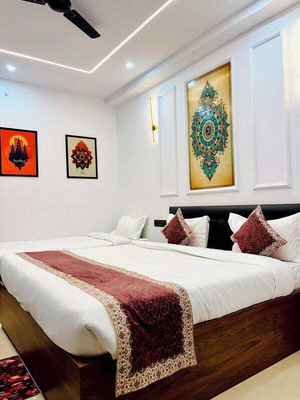A modern bedroom with a large bed, white bedding, and decorative pillows. There are wall-mounted artworks and a ceiling fan. - The Ravishya Retreat (Ayodhya)