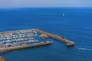 Eine Vogelperspektive auf eine Marina mit zahlreichen vertäuten Booten, einer Mole und einem Leuchtturm in der Ferne.