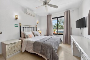 Ein Schlafzimmer mit einem Bett, Nachttischen, einem Deckenventilator, einem Fernseher und einem Fenster mit Vorhängen.