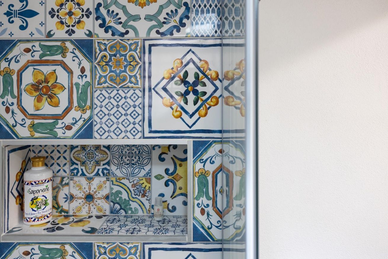 Een betegelde muur met verschillende patronen en een zeepfles.