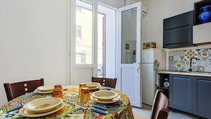 Comedor con mesa preparada para cuatro, cocina con salpicadero de azulejos y puerta que da a un espacio exterior.