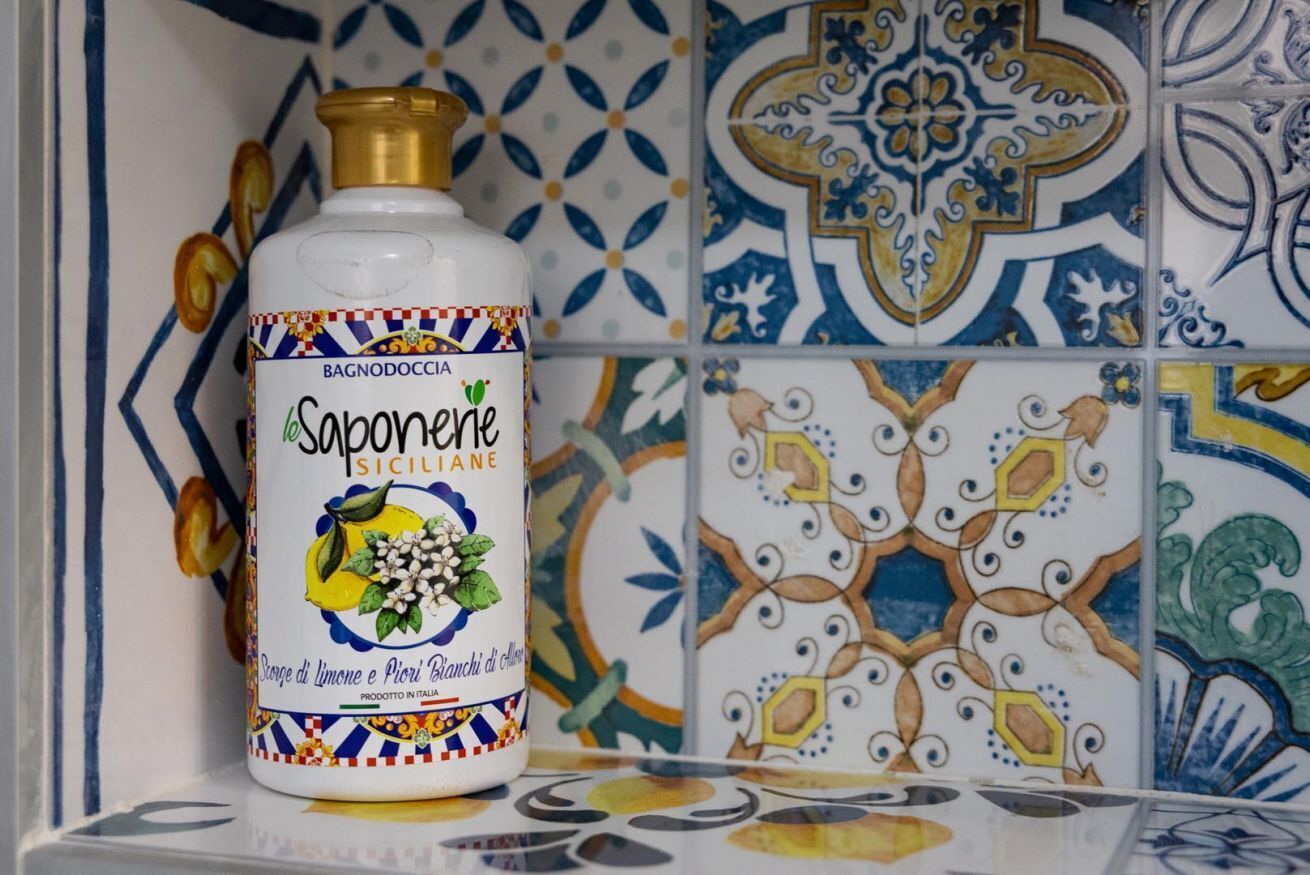 Una botella de jabón Bagnodoccia sobre una estantería con baldosas de cerámica coloridas.