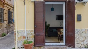 Una entrada residencial con un muro de piedra, una planta en maceta y una puerta que da a un interior con un sofá y una televisión.