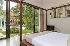 A bedroom with a bed, a television, a sliding glass door leading to a garden, and a painting on the wall.