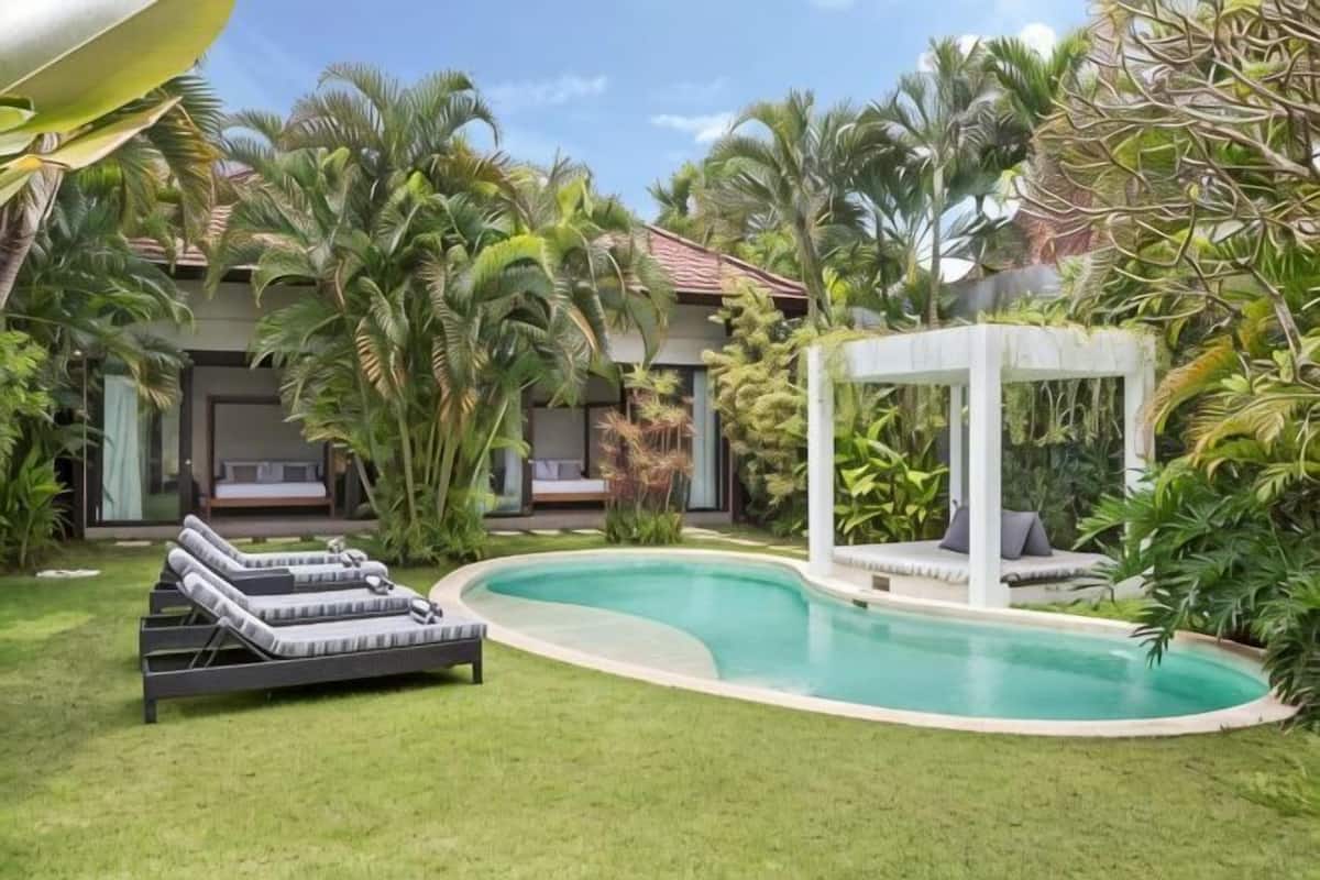 A pool with lounge chairs, a gazebo, and a building with a tiled roof.
