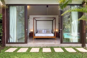 A bedroom with a four-poster bed, a glass door entrance, and a small bedside table. - Villa Alice Satu (Bali)