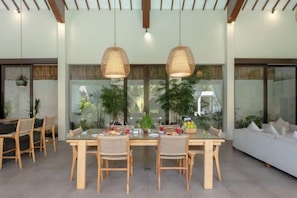 A dining area with a large table, wicker chairs, and hanging pendant lights. - Villa Alice Satu (Bali)