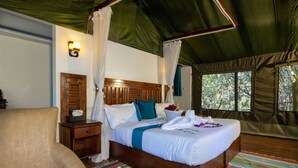 Ruime kamer met een groot bed, een houten nachtkastje, een stoel en een raam met uitzicht op bomen.