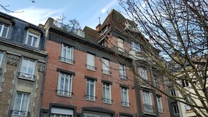 Ein mehrgeschossiges Gebäude mit einer Mischung aus Ziegel- und Natursteinfassaden, zahlreichen Fenstern mit Fensterläden und Balkonen.