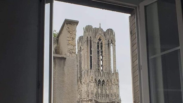 Blick durch ein Fenster auf eine gotische Kathedrale. Im Inneren sind ein Heizkörper und ein Stuhl zu sehen.