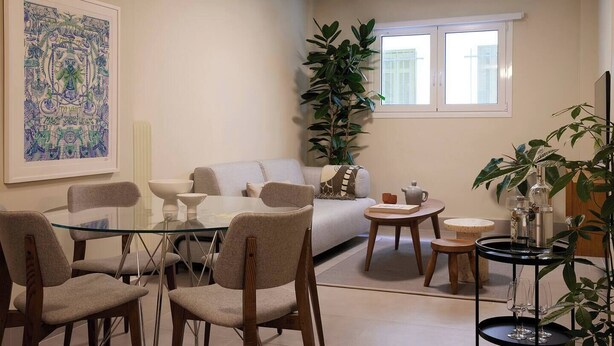 A modern living room with a glass dining table, comfortable seating, a large plant, and a window with blinds. - Phaedrus Living: Kolonaki Crown Residences 1 (Athens)