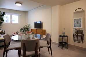 Ein modernes Wohnzimmer mit einem Glastisch, bequemen Sitzmöglichkeiten, einem Flachbildfernseher, einer Holzkommode und einem großen Spiegel.