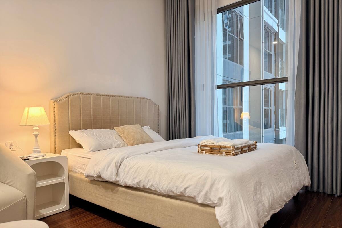 Une chambre d’hôtel avec un grand lit, une table de chevet avec une lampe, une chaise et une vue sur un immeuble par la fenêtre.