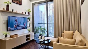 Een moderne woonkamer met een flatscreen televisie, een bank, een salontafel en een balkon met uitzicht op hoge gebouwen.