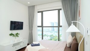 Een moderne hotelkamer met een groot raam, een flatscreen televisie, een bedlampje en een opgemaakt bed.