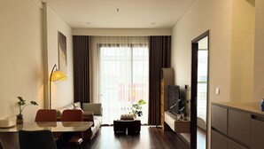 Een moderne hotelkamer met een zithoek, een bank, een televisie en een groot raam met gordijnen.