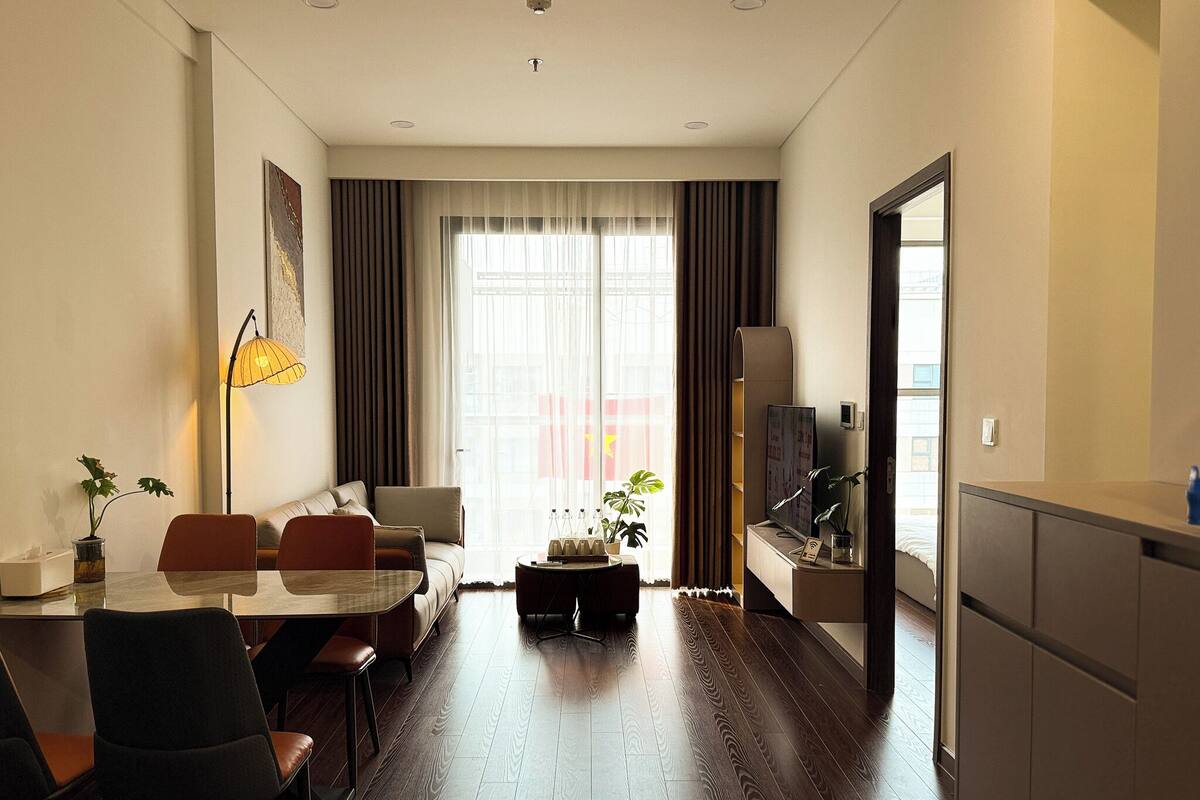 Une chambre d’hôtel moderne dotée d’un coin repas, d’un canapé, d’une télévision et d’une grande fenêtre avec des rideaux.