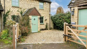 A stone house with a green door, a gravel driveway, and a wooden gate. - Beautiful 3 Bedroom Cotswold Cottage (Chipping Norton)