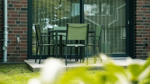 Eine Terrasse mit Tisch und Stühlen, eine Glastür und eine Ziegelwand.