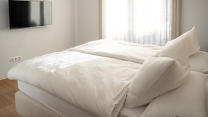 Ein modernes Schlafzimmer mit einem Bett, einem flachbildfernseher an der Wand und einem Fenster mit transparenten Vorhängen.