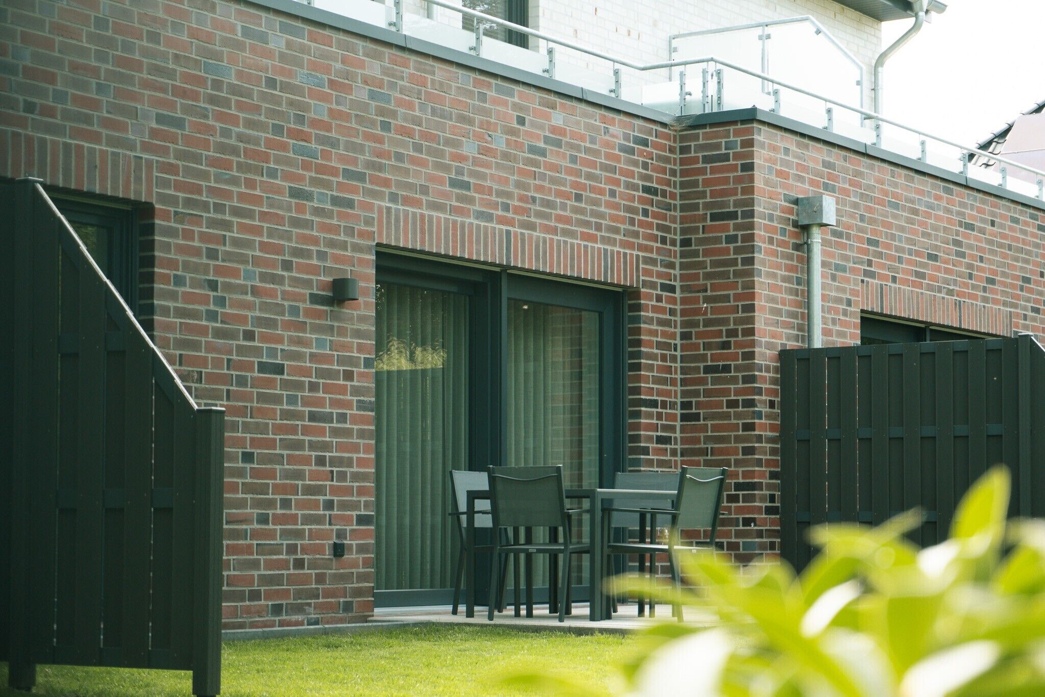 A brick building with a patio area, including a table and chairs, and a fenced garden.