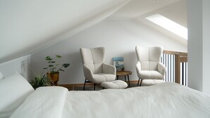 Ein Schlafzimmer mit schrägverlaufender Decke, zwei Sesseln, einem kleinen Tisch und einer Topfpflanze.