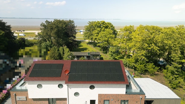 Ein modernes Gebäude mit rotem Dach, Solaranlagen und Blick auf einen See.