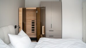 Un dormitorio moderno con cama, almohadas blancas, pared de paneles de madera, armario y luz empotrada.