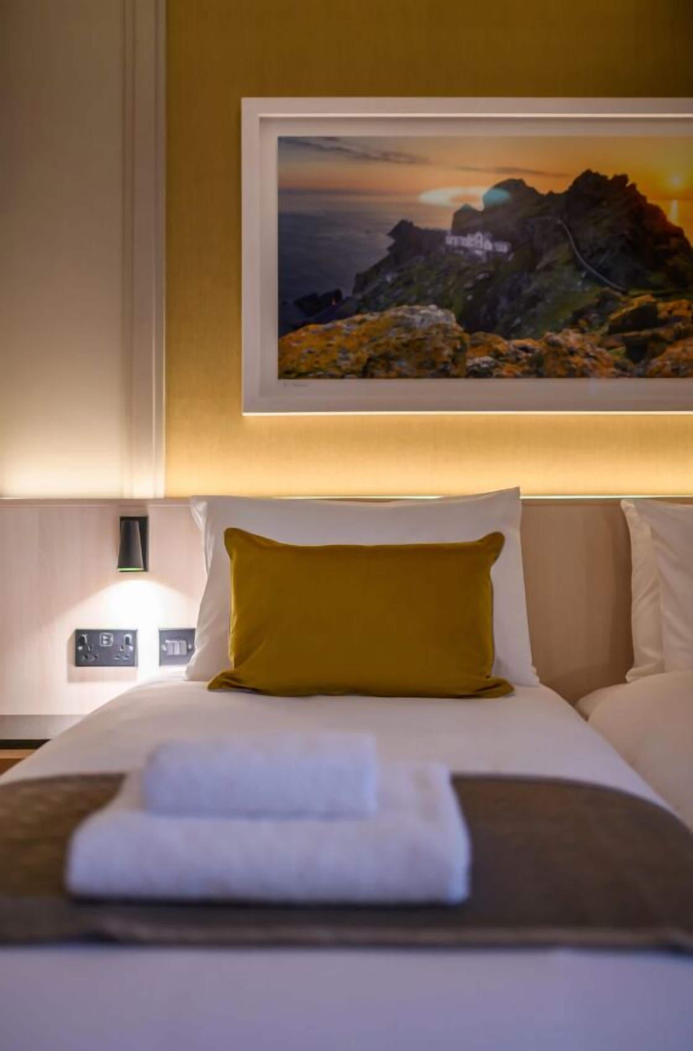 A hotel room with a bed, a framed picture on the wall, a nightstand, and a lamp.