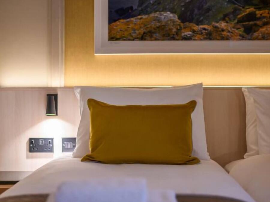 A hotel room with a bed, a framed picture on the wall, a nightstand, and a lamp.