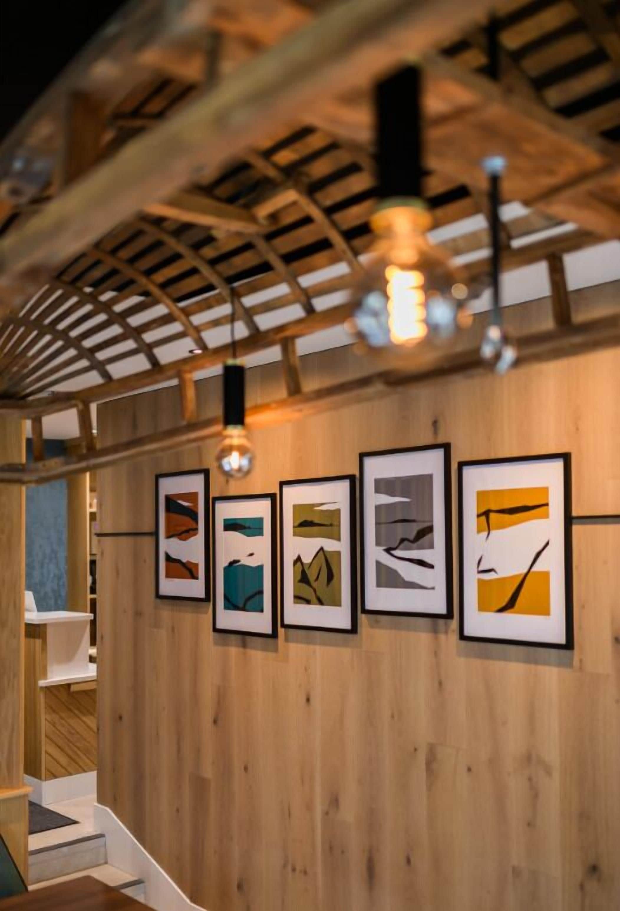 Un intérieur en bois avec un escalier, des œuvres d’art encadrées au mur et un luminaire suspendu.