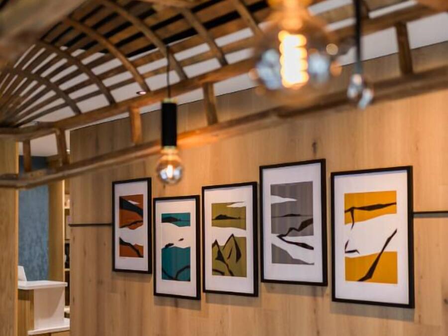 A wooden interior with a staircase, framed artwork on the wall, and a hanging light fixture.