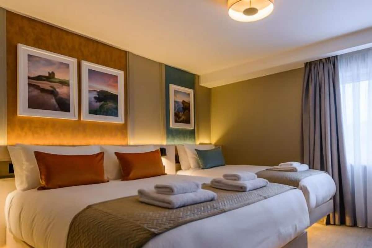 A large bed with multiple pillows and a blanket, a bedside table, and wall-mounted artwork.