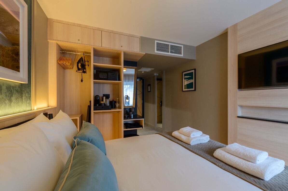 A hotel room with a bed, a walk-in closet, a mirror, and a TV.