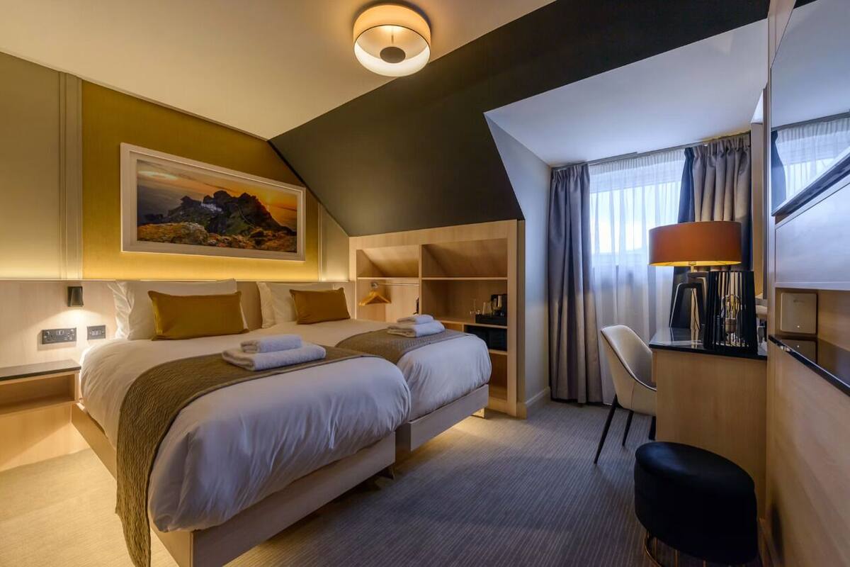 A hotel room with a bed, bedside tables, a desk, a chair, a lamp, and a painting on the wall.