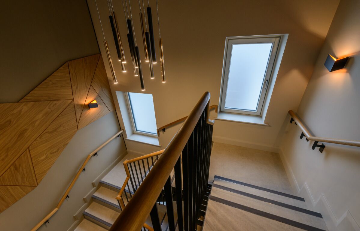 A modern staircase with wooden steps, black handrails, and pendant lighting.