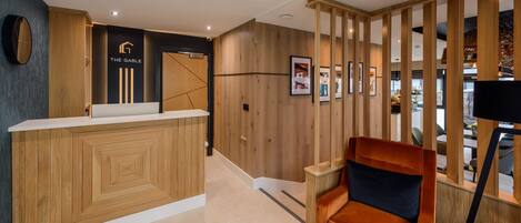 A reception desk with a wooden finish, a black wall with a logo, and a wooden partition.