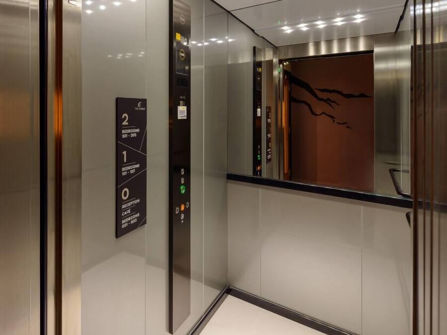 Interior de ascensor con indicadores digitales de piso, una señal en la pared con números de piso y una puerta metálica con un panel decorativo marrón.