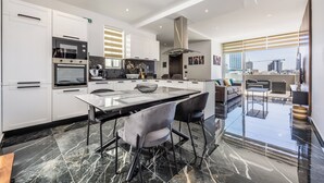 A modern kitchen with white cabinets, a black countertop, and a dining area with a glass table and chairs. - 1 BR Penthouse for Couples & Families (Pembroke)