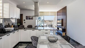 A modern kitchen with white cabinets, a black countertop, and a dining area with a marble table and black chairs. - 1 BR Penthouse for Couples & Families (Pembroke)