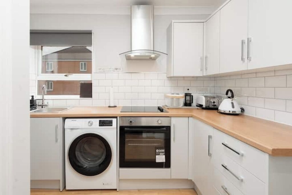 A compact kitchen with a washing machine, oven, and a coffee maker on the countertop.