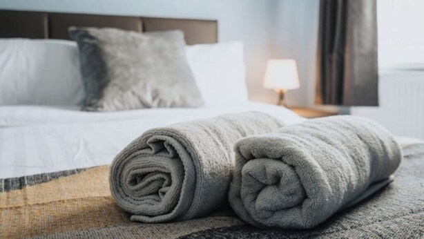A neatly made bed with a rolled-up gray towel and a pillow on a textured bedspread. - Comfort & Convenience in Telford – Cozy 3-Bedroom Home (Telford)