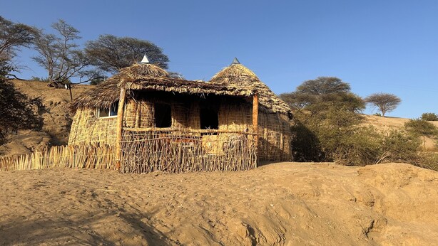A thatched-roof hut with a simple, open structure, surrounded by dry, sandy terrain and sparse vegetation. - Eliye Springs Resort (Eliye)