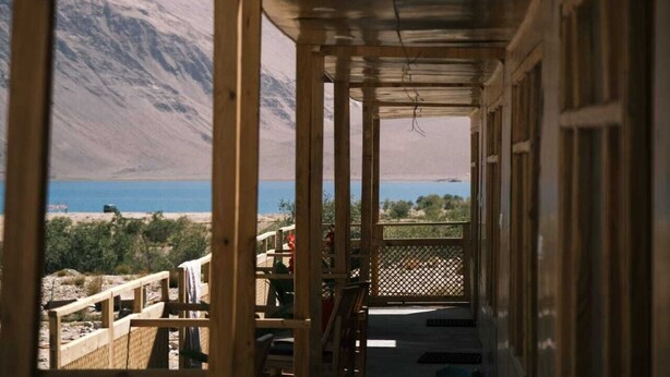 A wooden balcony with a view of a lake and mountains. - Wilderness Retreat (Leh)