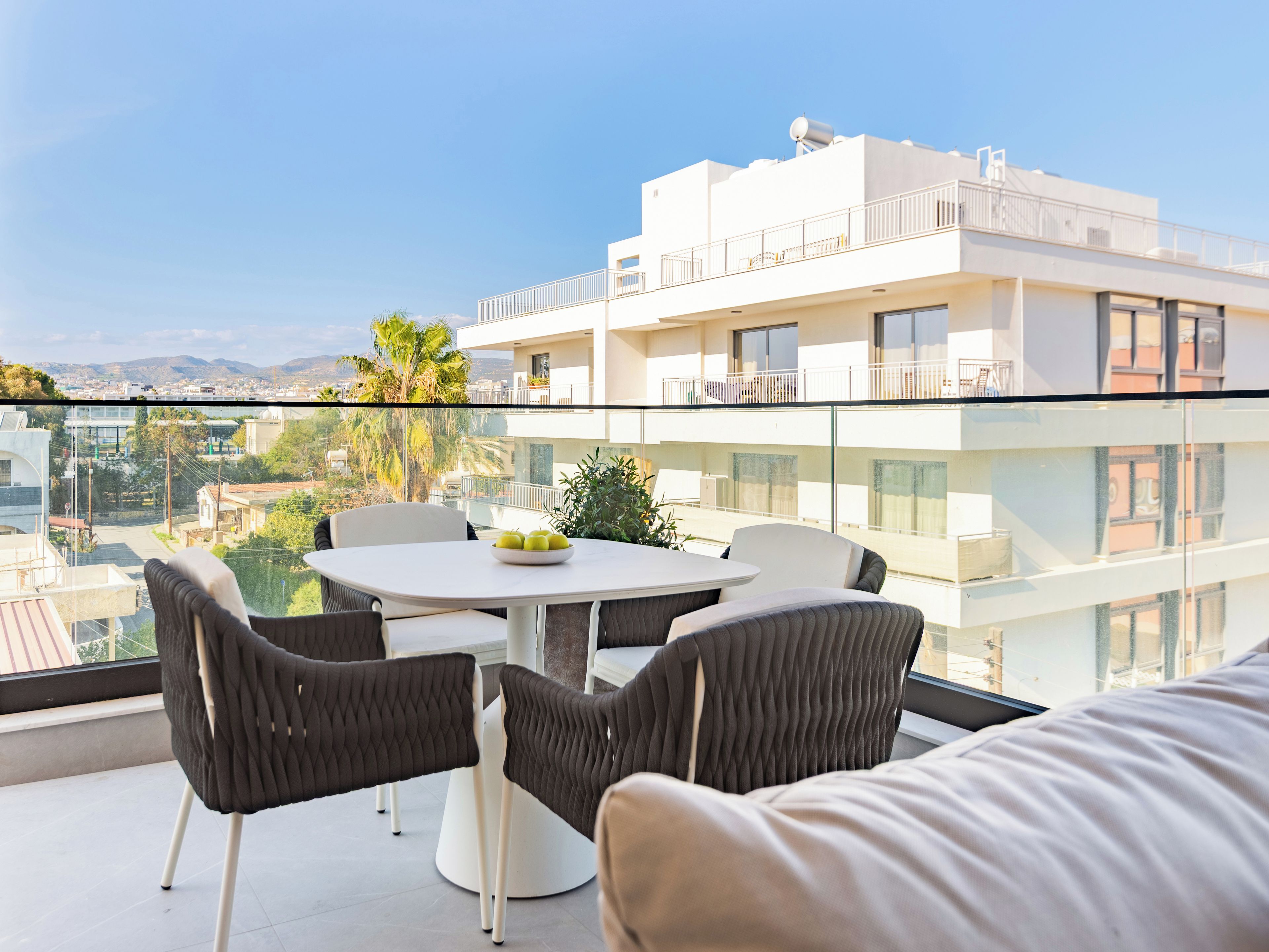 A balcony with a table and chairs, a white building in the background, and a view of the city.
